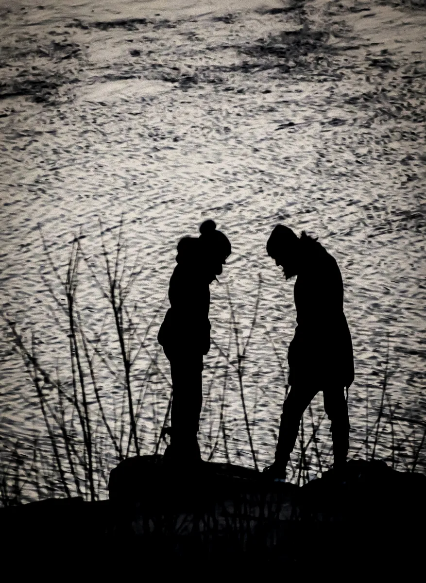 Two human silhouettes facing each other against shimmering water